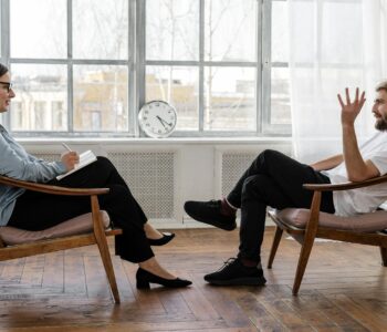 person in black pants and black shoes sitting on brown wooden chair